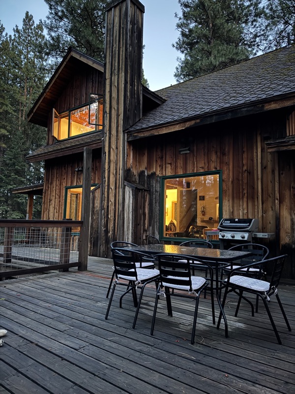 The cabin's wood deck with dining table, chairs and propane grill beside lit glass doors