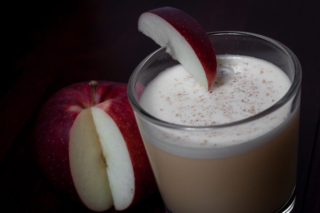 A glass of apple cider garnished with an apple slice and cinnamon